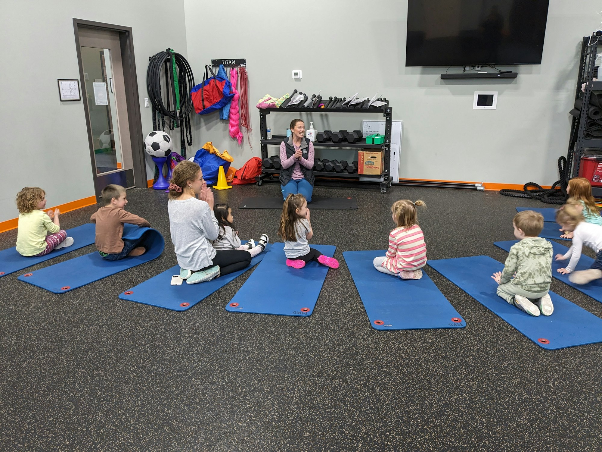 Children sitting on mats, participating group activity led by instructor Danielle Musser