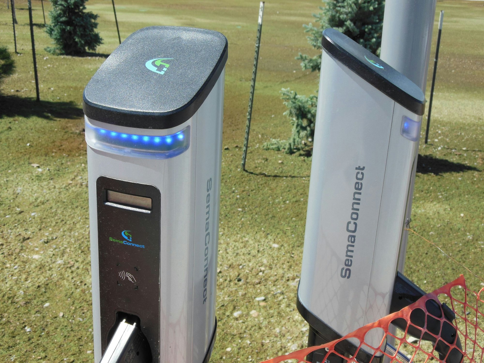 The image shows SemaConnect electric vehicle charging stations with blue lights, set in a grassy outdoor area.