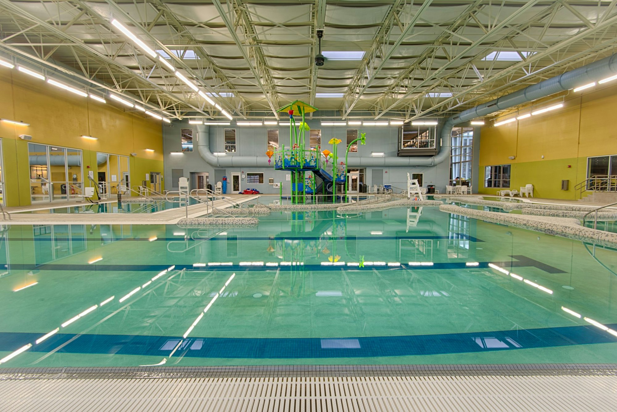 An indoor swimming pool area featuring slides, a lifeguard station, and bright lighting.