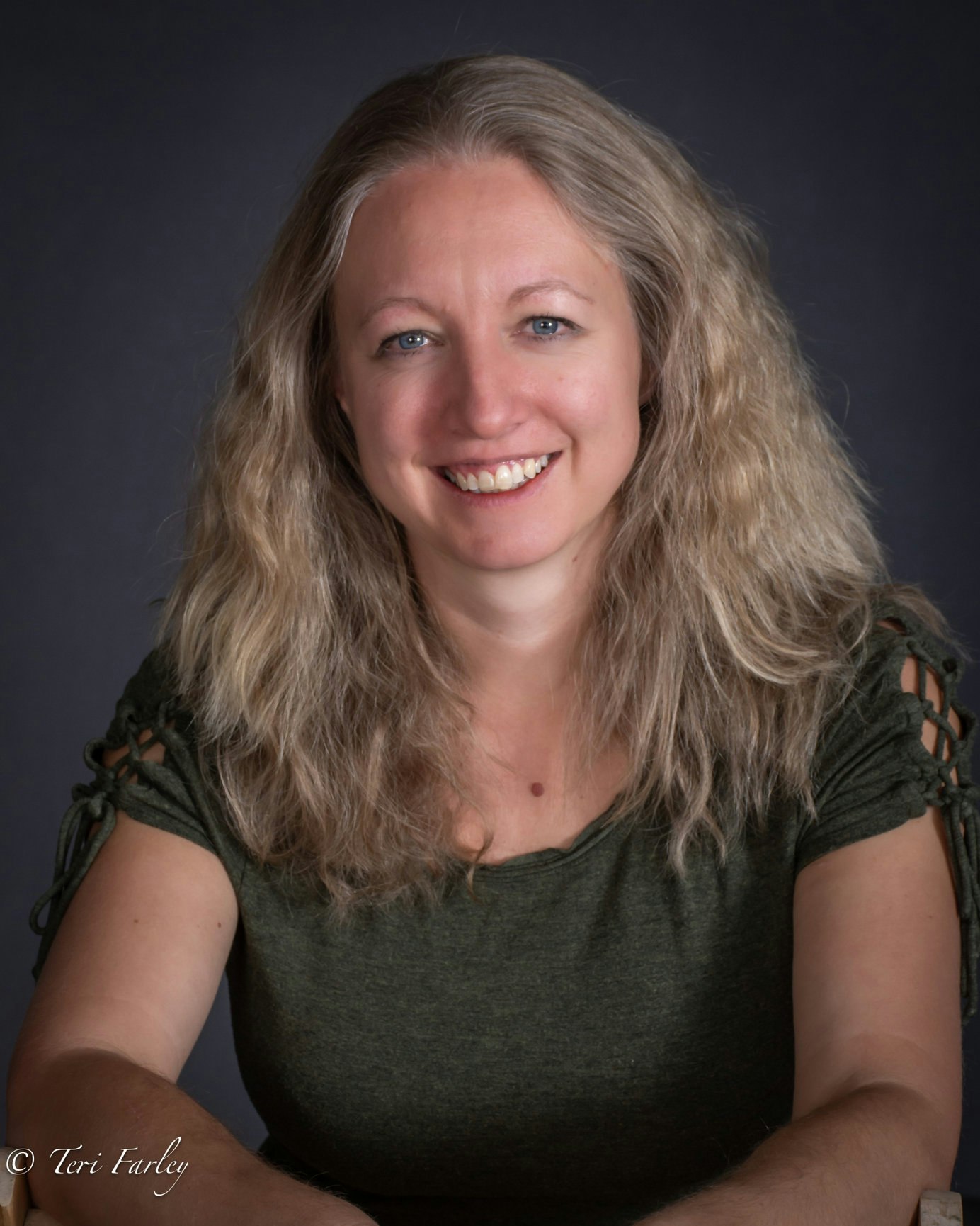 A smiling woman with blond hair, green top, against a dark backdrop.