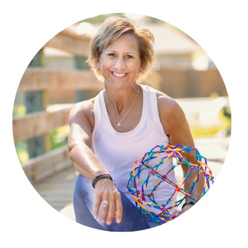 A person sitting on a wooden structure, smiling, holding a colorful plastic sphere, wearing a white tank top and necklace.