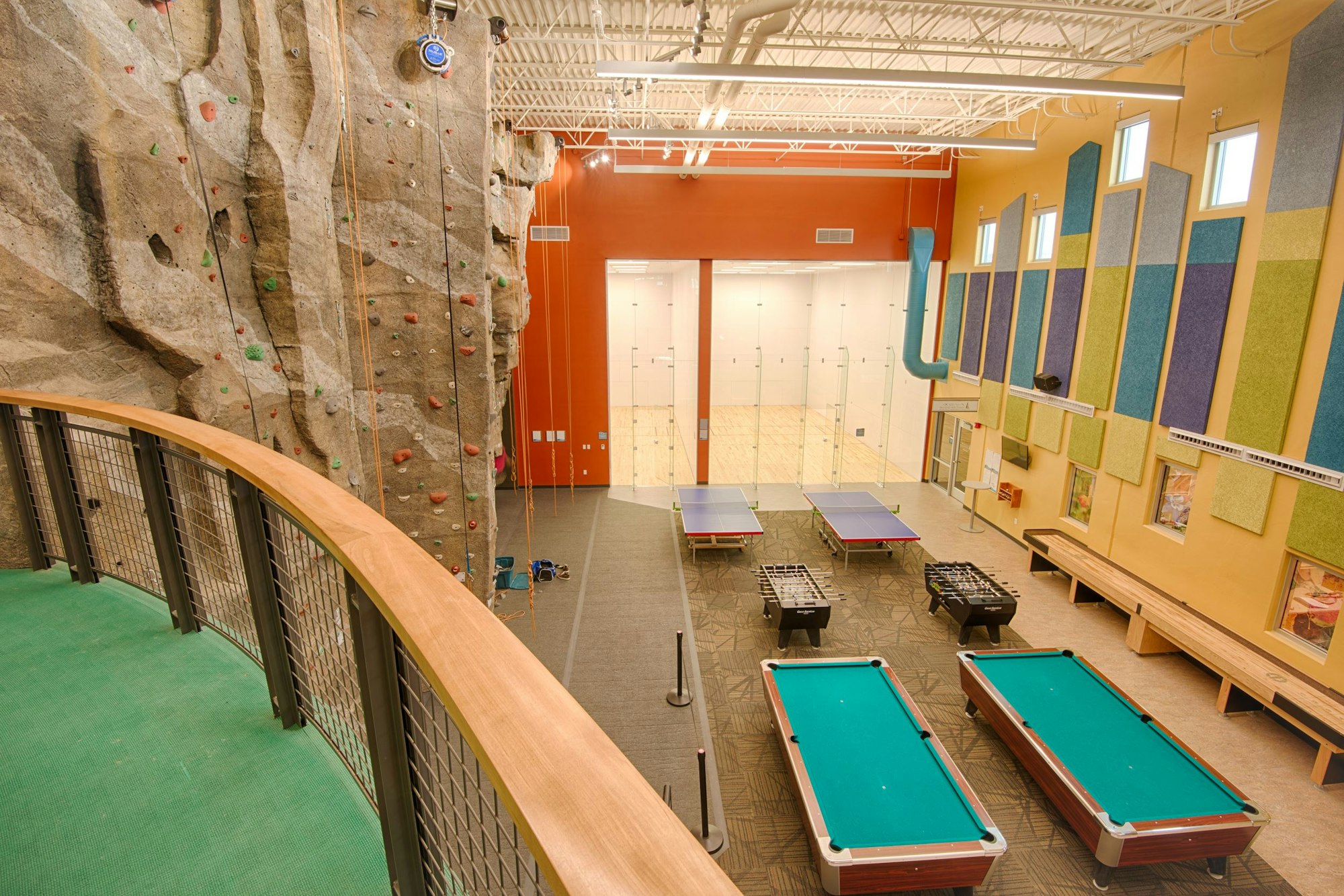 A spacious activity center featuring a rock climbing wall, ping pong tables, pool tables, and racquetball courts.