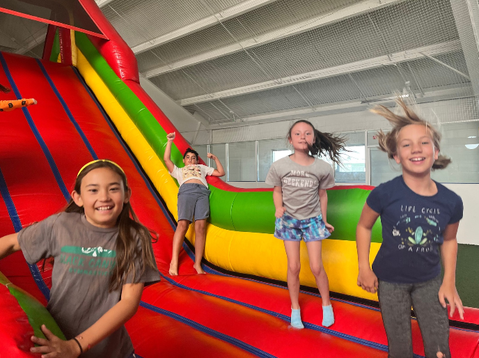 Children playing on a colorful inflatable bounce house indoors.