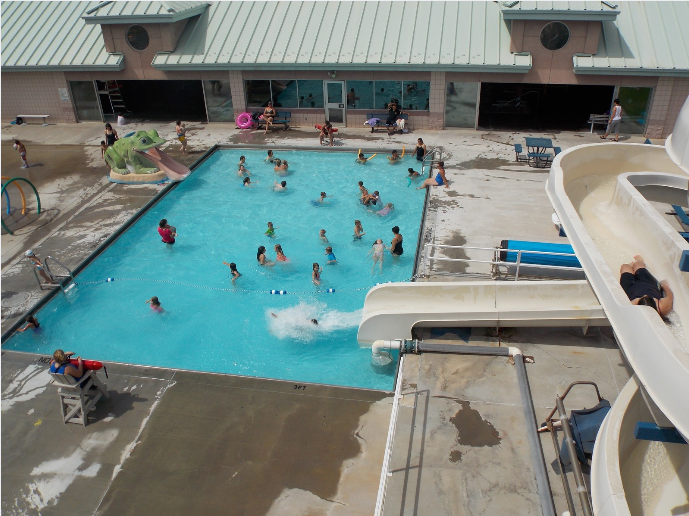 A swimming pool with people, slides, and lounging areas.