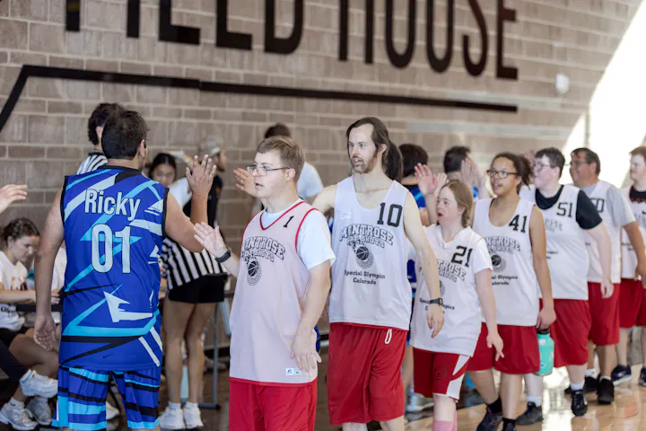 Participants in a basketball event are high-fiving and celebrating, wearing jerseys, showcasing teamwork and camaraderie.