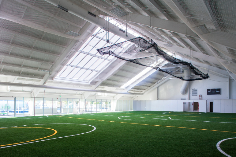 Indoor sports facility with artificial turf, skylights, and a soccer goal.
