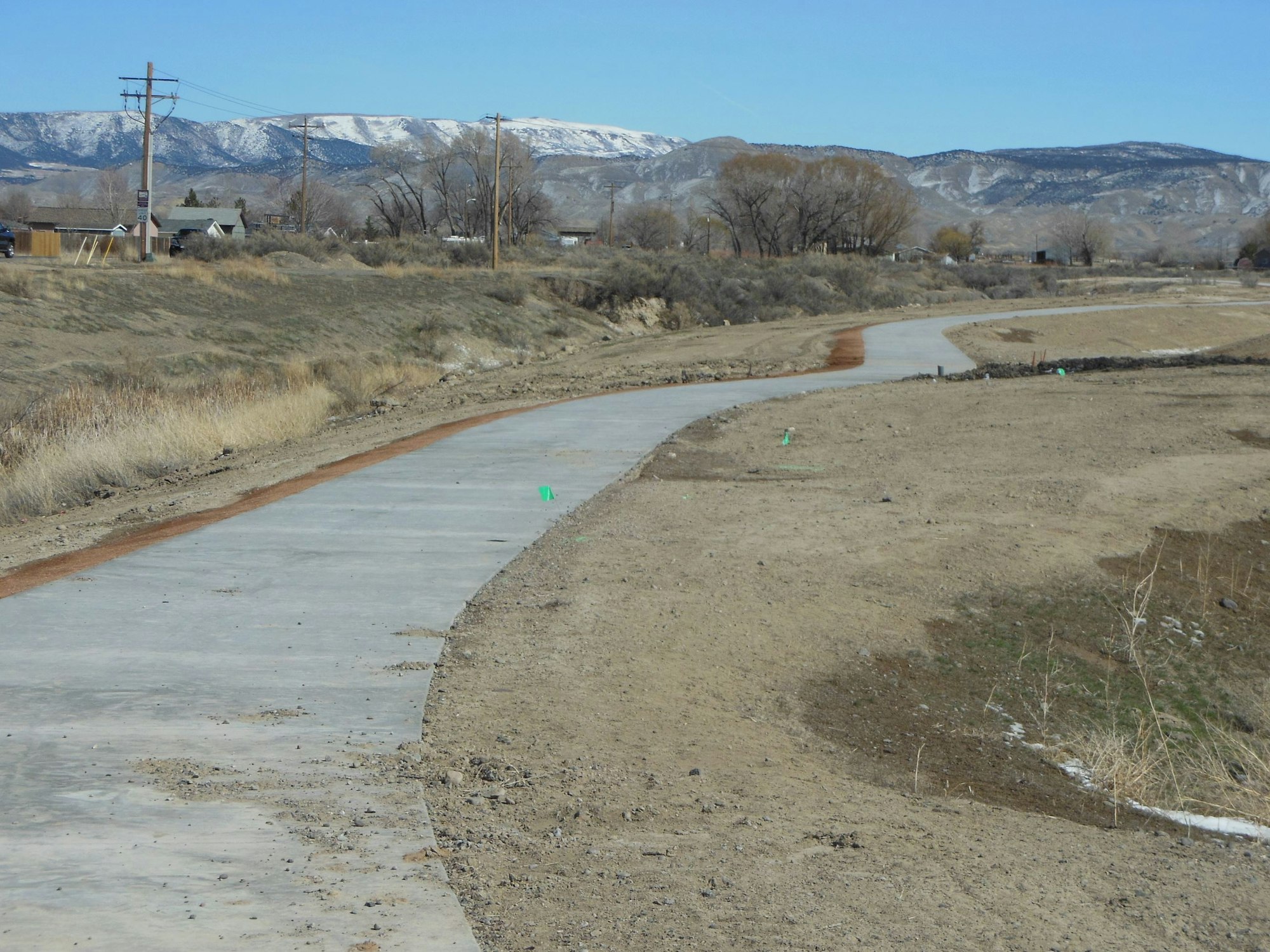 A winding concrete path stretches through a dry area, with mountains in the background and sparse vegetation nearby.