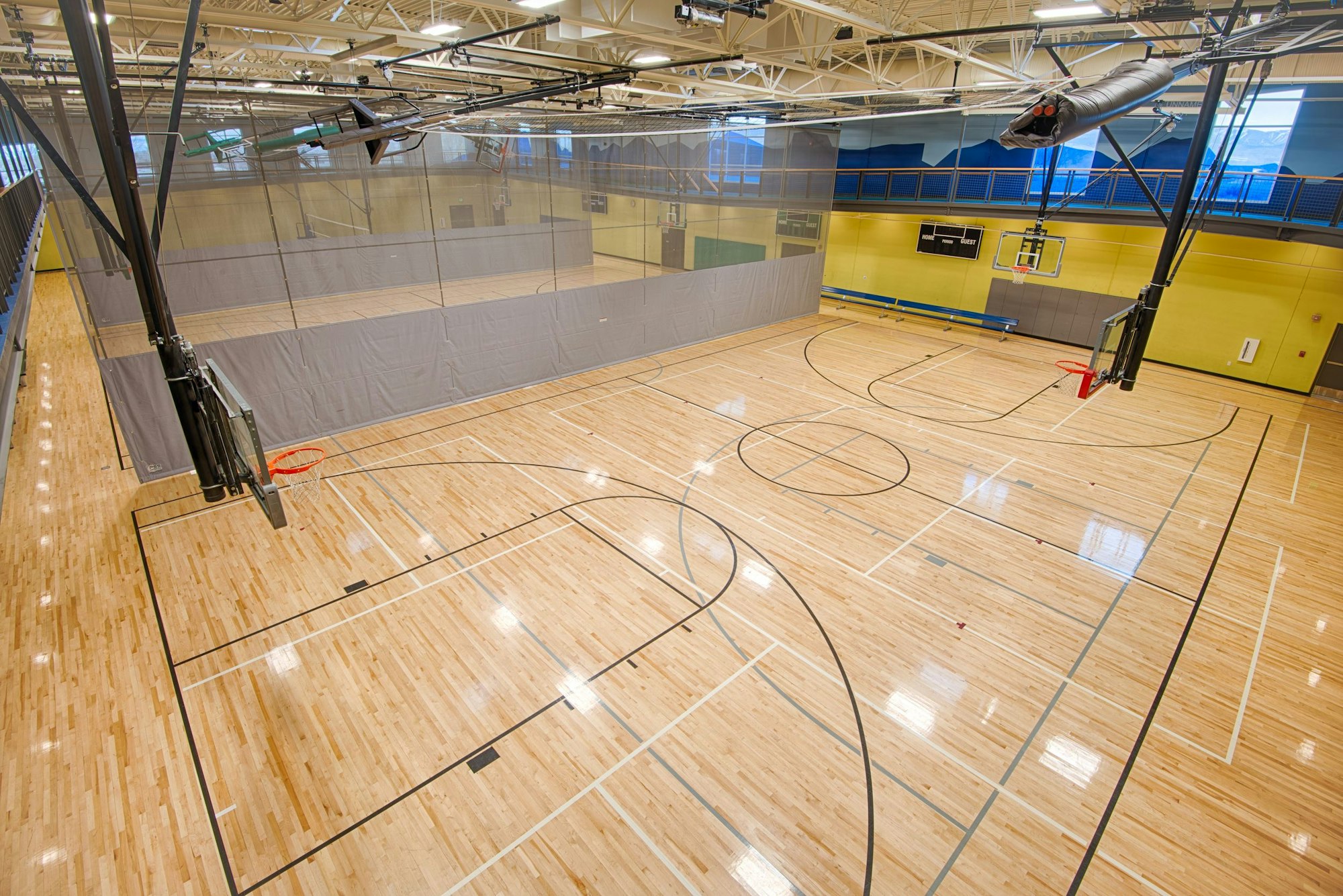An indoor basketball court with polished wooden floors, basketball hoops, and dividing curtains. Bright and spacious environment.