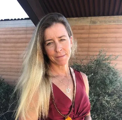 A smiling woman in a maroon top and patterned skirt, outdoors, image rotated 90 degrees.