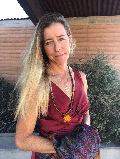 A smiling woman in a maroon top and patterned skirt, outdoors, image rotated 90 degrees.