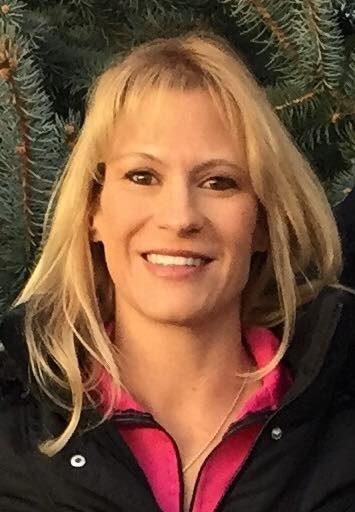 A smiling woman with blonde hair in front of a tree.