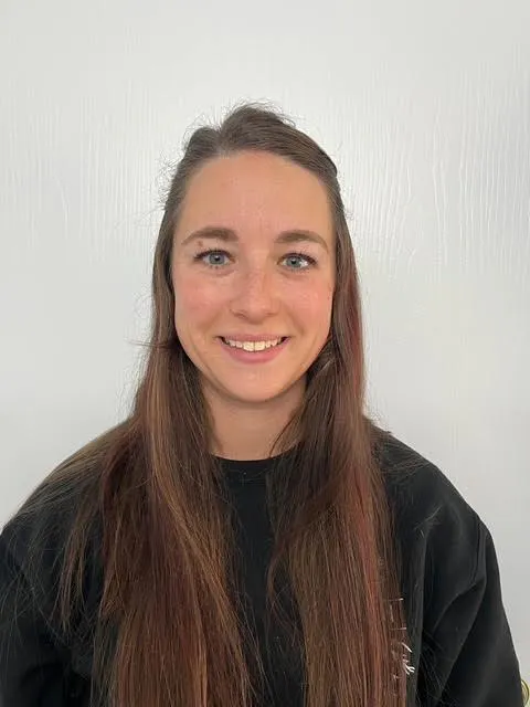 A smiling person with long hair, wearing a black sweatshirt, poses in front of a white background.