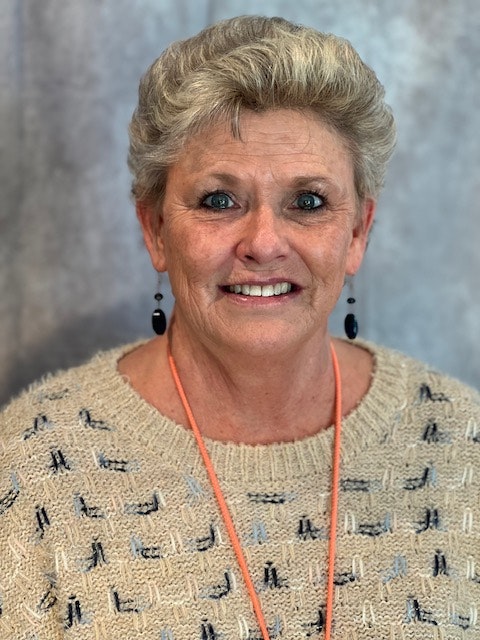 Portrait of a smiling woman with short hair, wearing earrings, a necklace, and a cream-colored sweater.