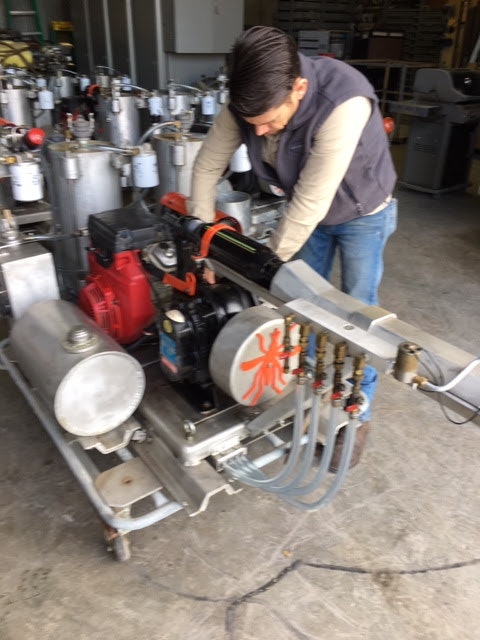 A person working on industrial machinery with multiple valves and metal tanks in a workshop.