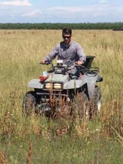 A person riding an ATV through a grassy field under a clear blue sky.