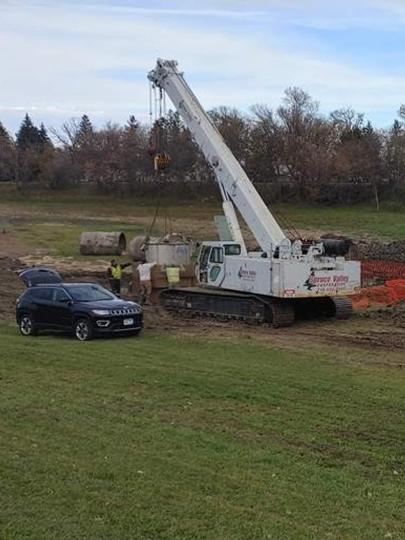 A crane lifting materials at a construction site with a car nearby.