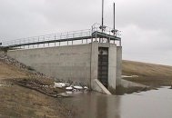 A concrete dam structure with water flowing through an outlet, mostly overcast sky.