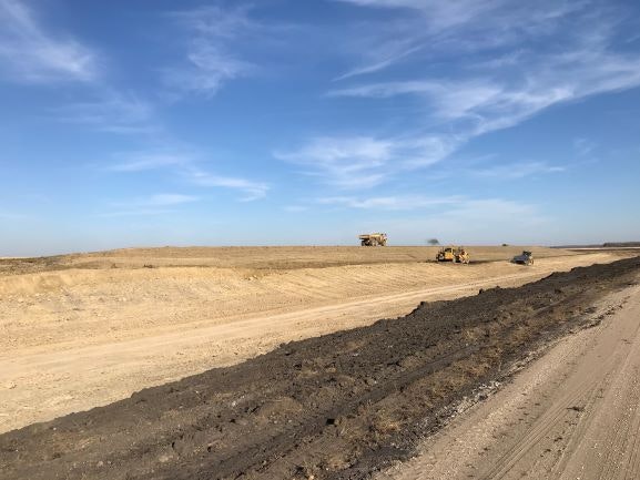 Construction vehicles on a dirt road under a blue sky with scattered clouds.