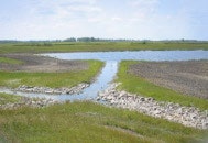 A small stream flows through grassy wetlands under a partly cloudy sky.