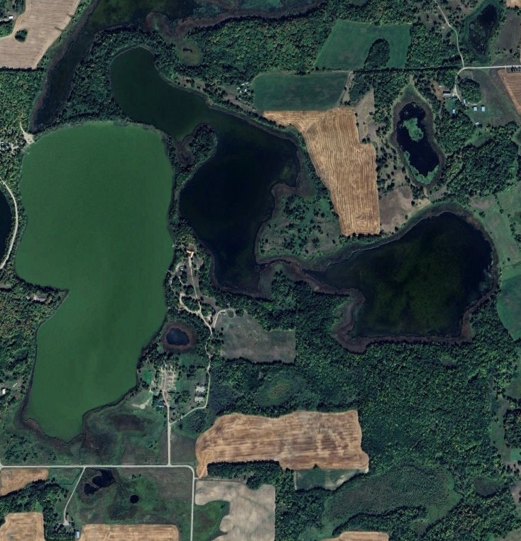 Aerial view of lakes, fields, forests, and a few scattered buildings and roads.