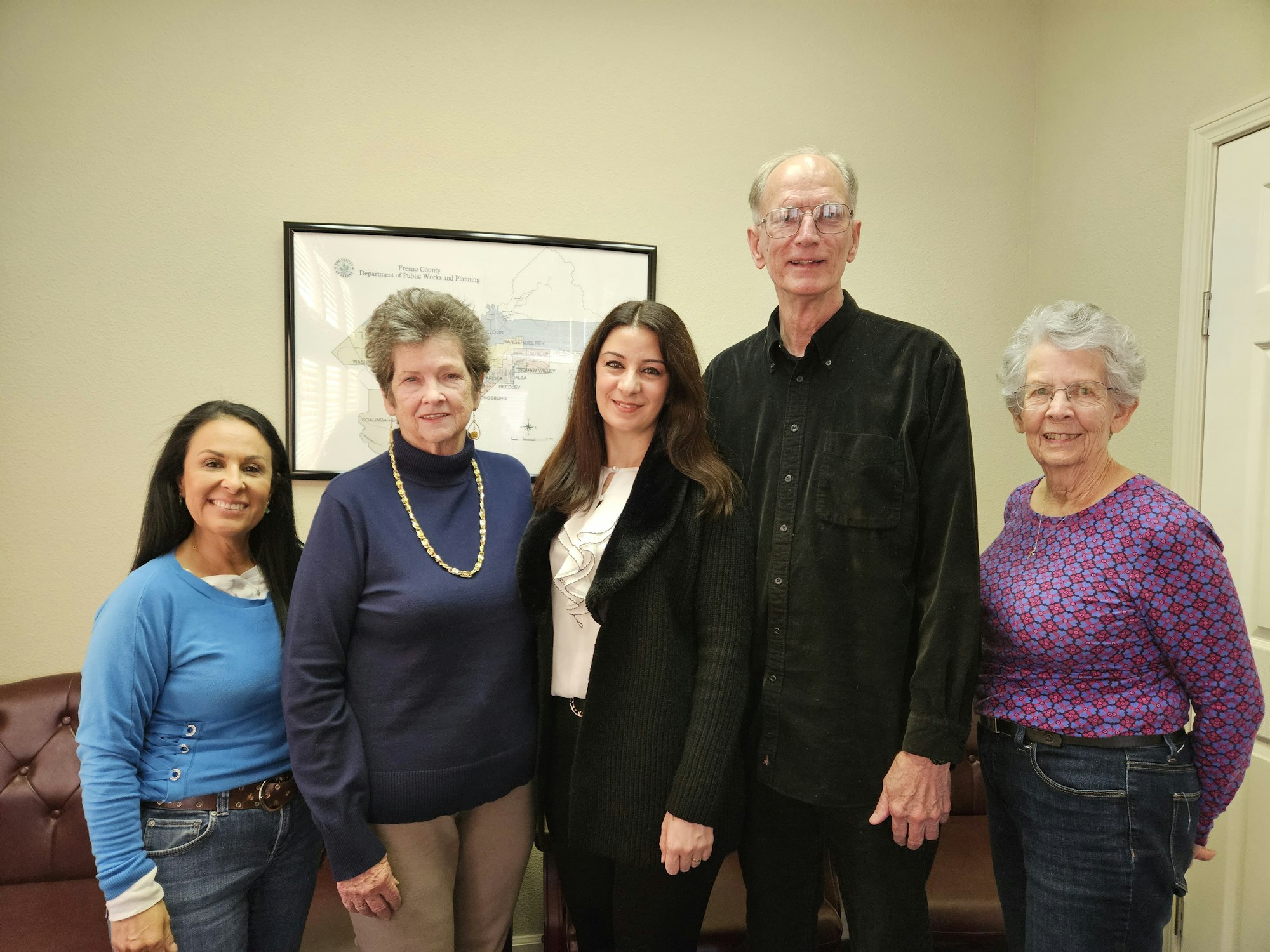 Five adults posing for a photo in a room with a framed document on the wall.