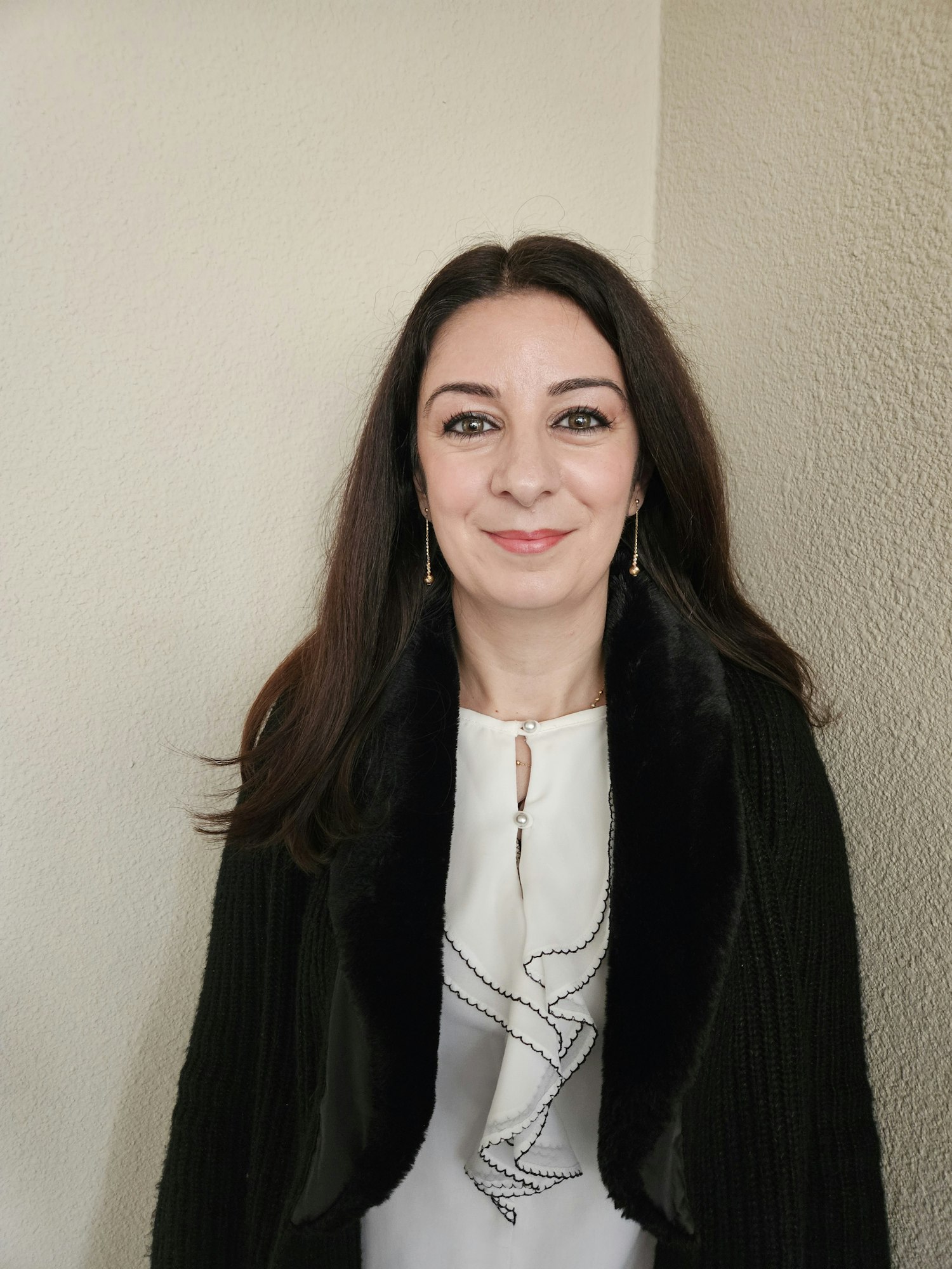 A smiling woman in a white blouse and black cardigan, standing against a plain background. Image is rotated 90 degrees.