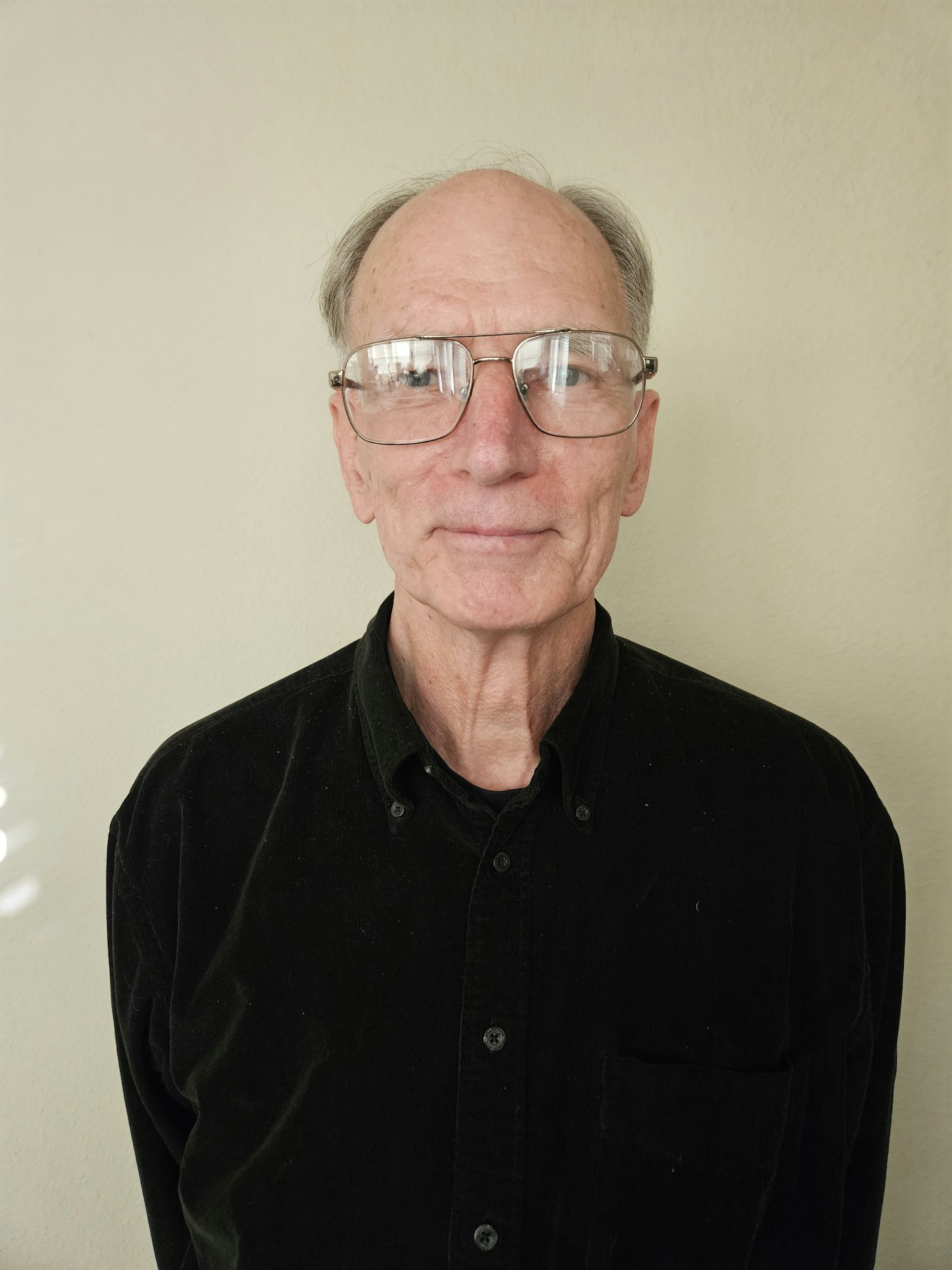 An elderly man with glasses wearing a black shirt, image rotated to the right.