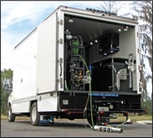 A white truck with the back open, equipped with machinery and a hose connected to equipment inside.