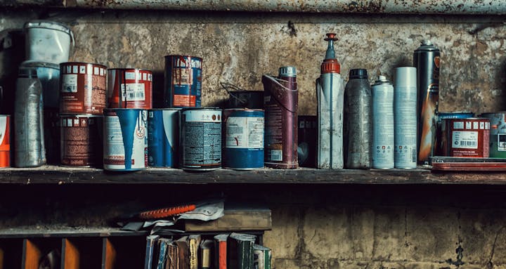 A shelf with various paint cans and spray bottles in a workshop.