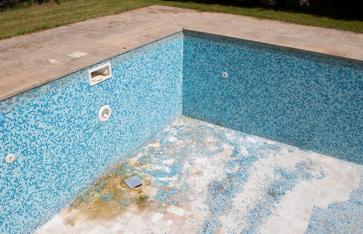 An empty swimming pool with blue tiles, some of which are damaged or missing.