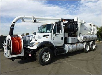 A large white vacuum truck with a hose reel and multiple tank compartments parked on pavement.