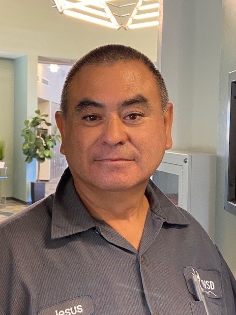 A man in a gray shirt smiling indoors.