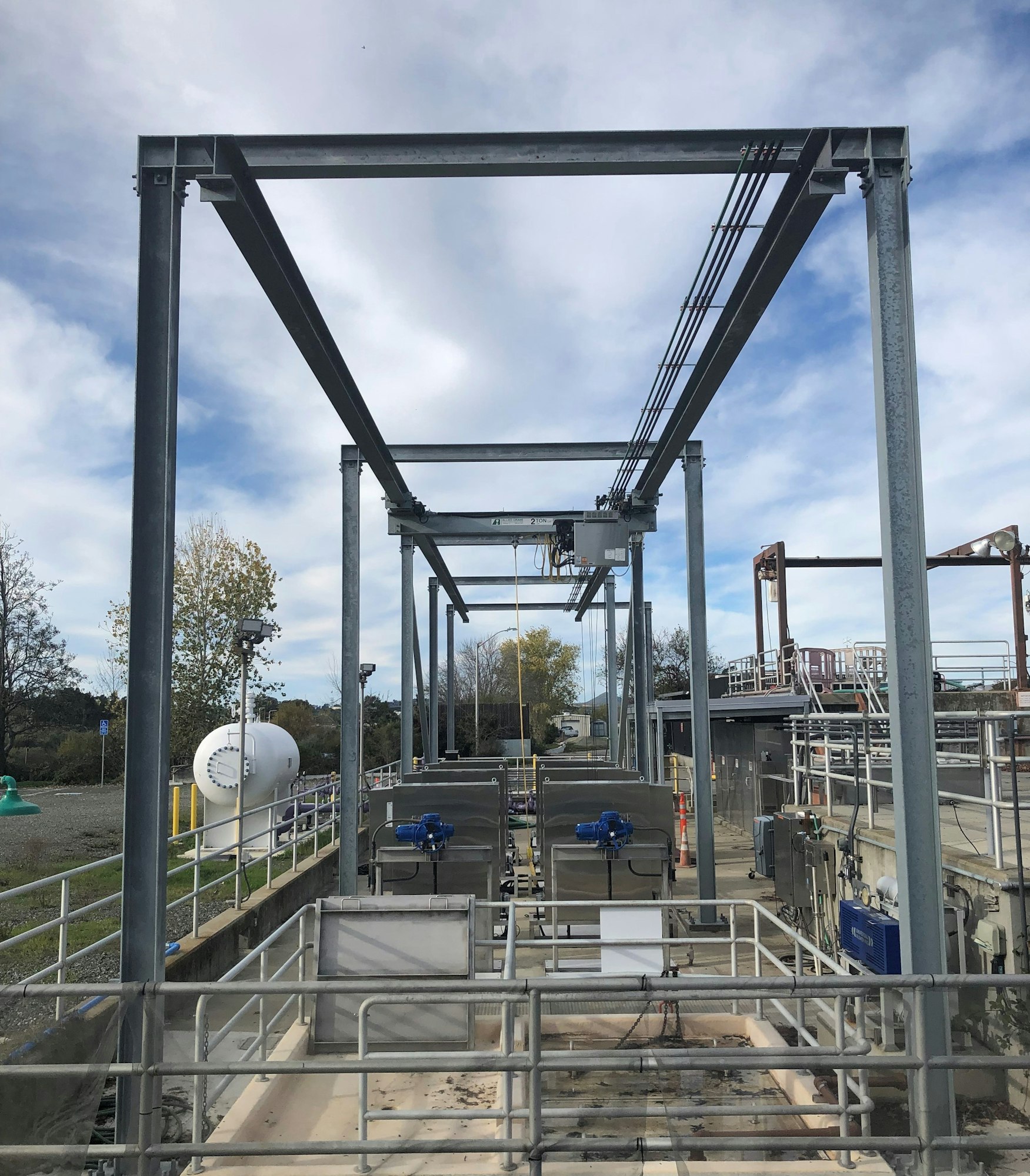 Industrial facility with metal structures, pipes, and tanks under a cloudy sky.