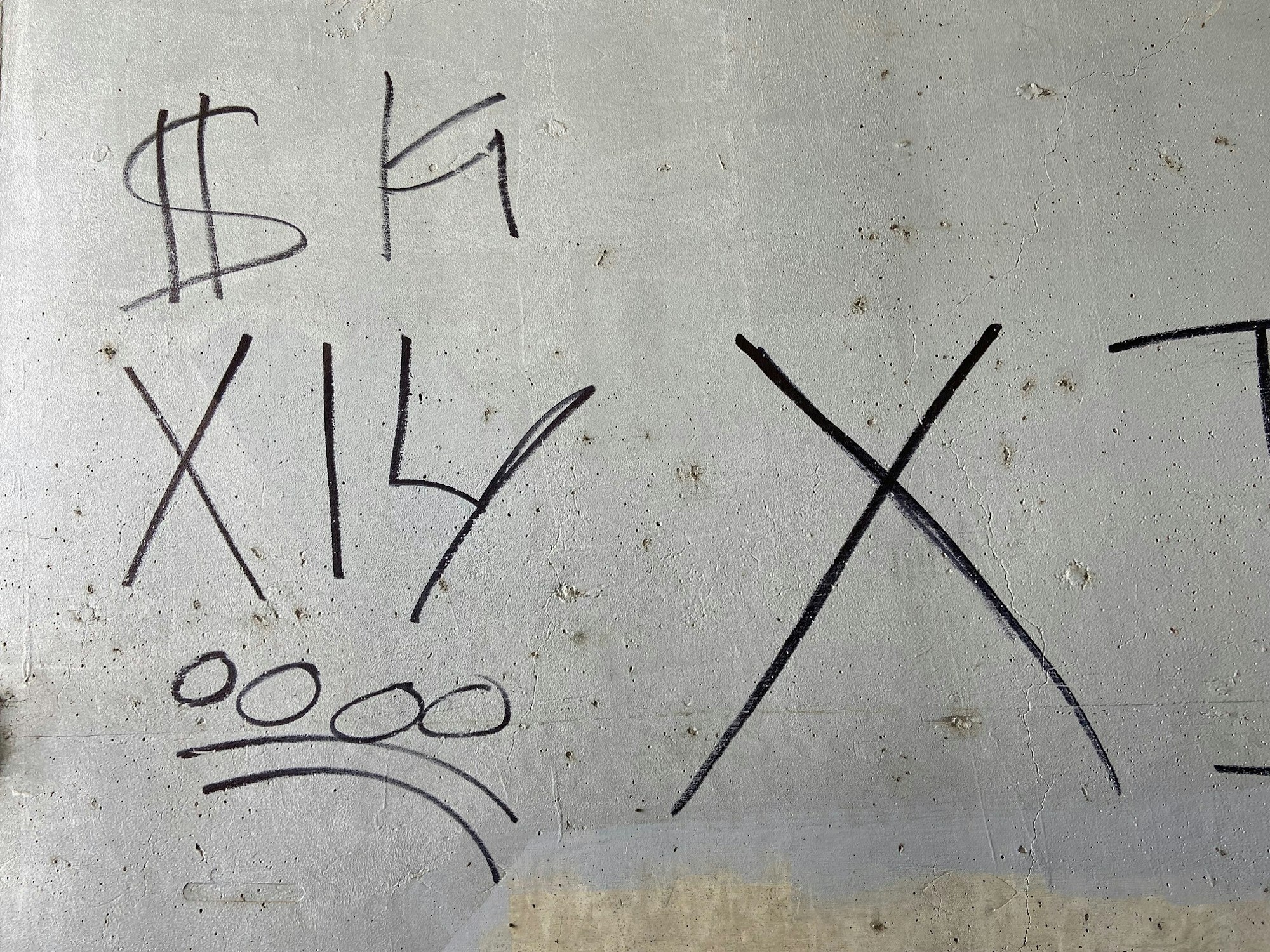 Graffiti on a wall with symbols: $, X, 14, and a sad face with three circles and lines.