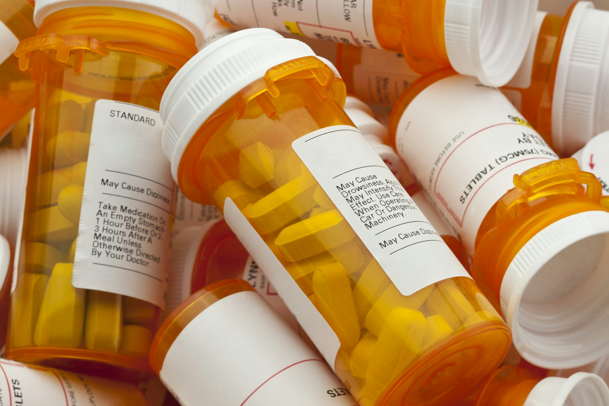 Pile of prescription medication bottles with labels and safety warnings.