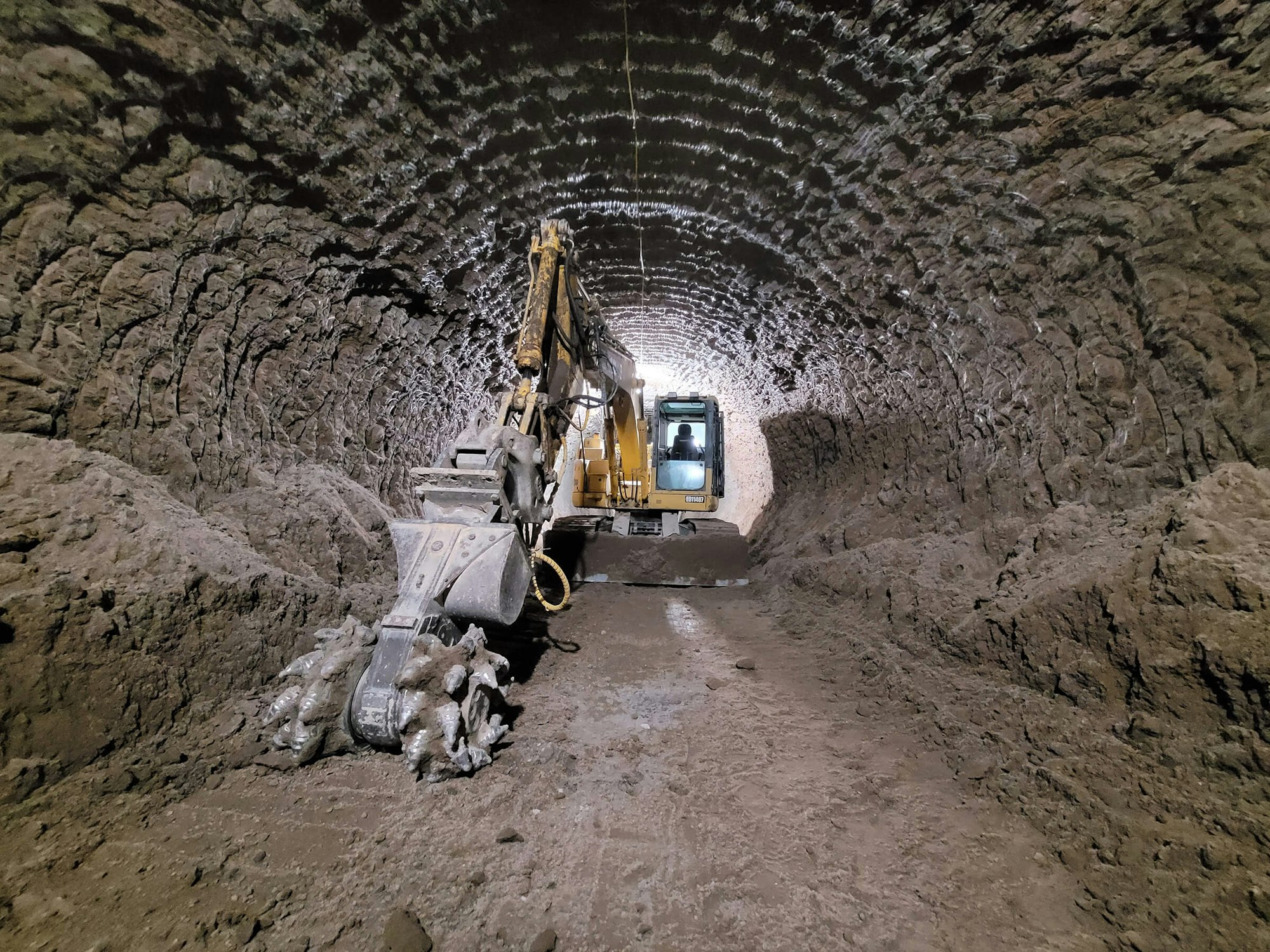 Excavator in a rocky tunnel, digging and clearing debris.