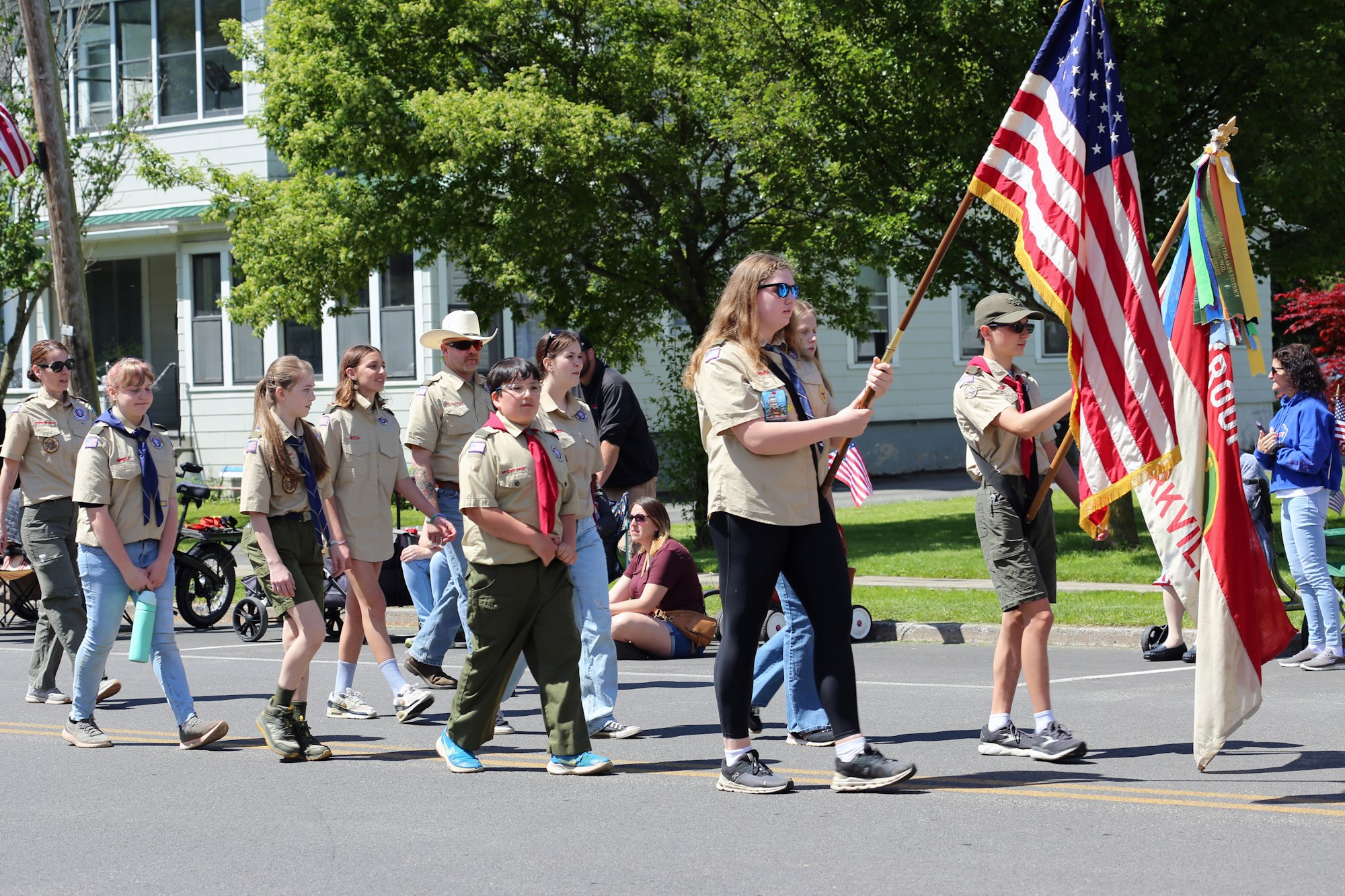 A group of scouts marching in a parade, holding American and troop flags.