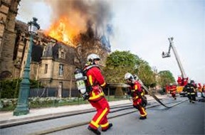 Firefighters combat a blazing fire at Notre Dame cathedral, using hoses and ladders to contain the flames.