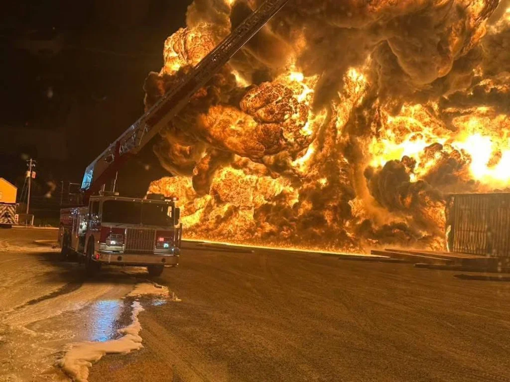 A large fire with a fire truck using a ladder to combat the flames.