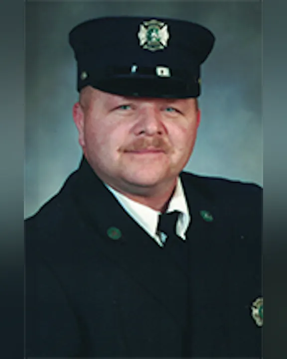 Charlie Spratt wearing a firefighter's uniform with a cap, looking at the camera.