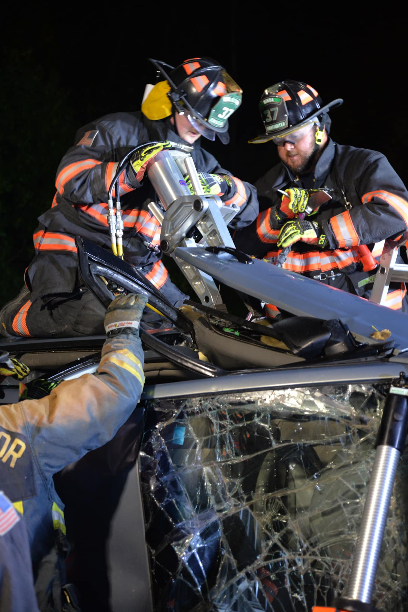 Firefighters using hydraulic tools at a car accident scene at night.