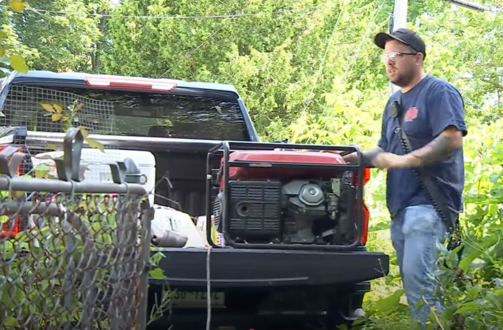 Firefighter beside a pickup truck with a generator in the truck bed, surrounded by trees and foliage.