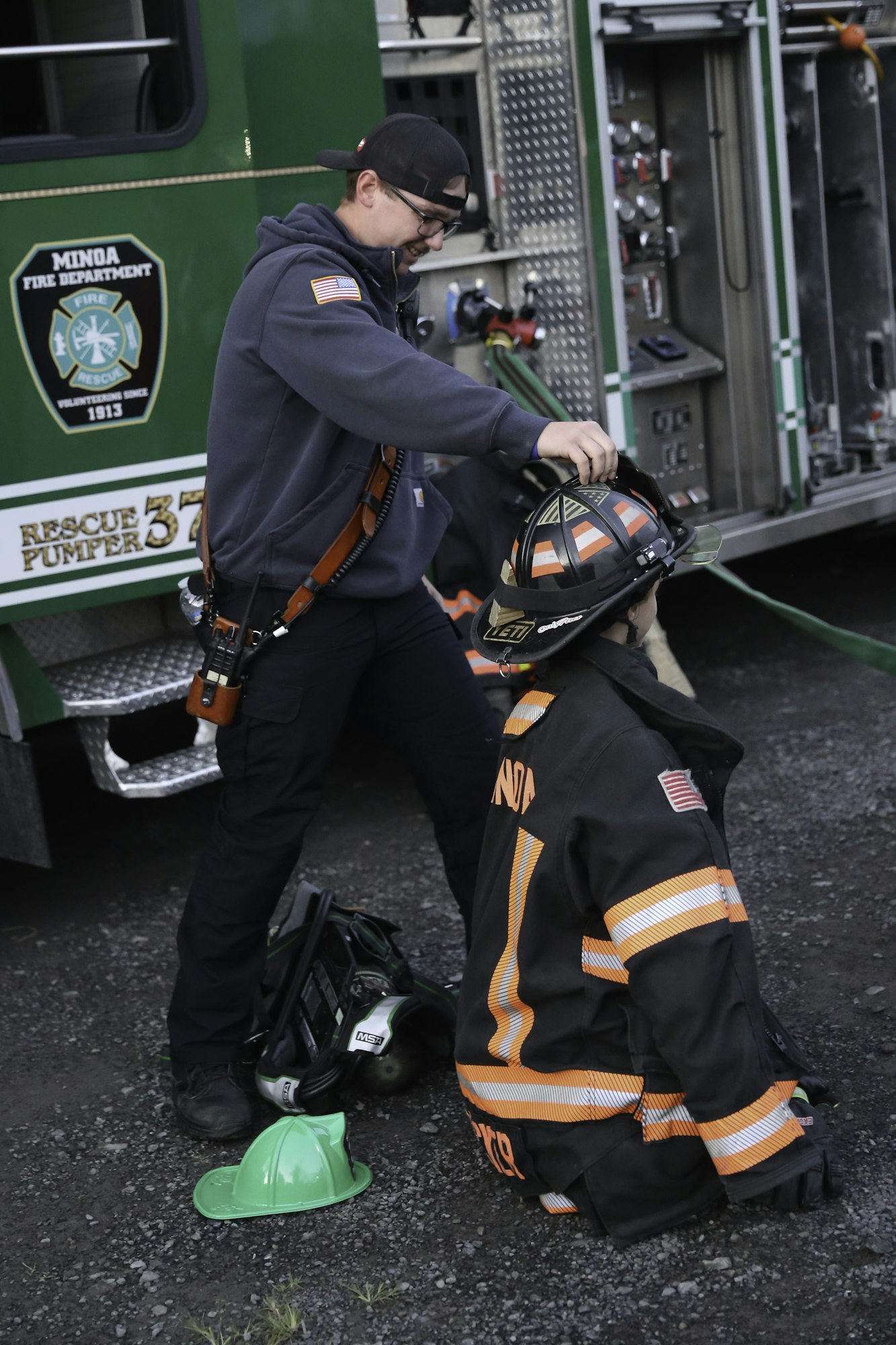 A firefighter adjusts a child's helmet beside a fire engine, indicative of a community or educational event.
