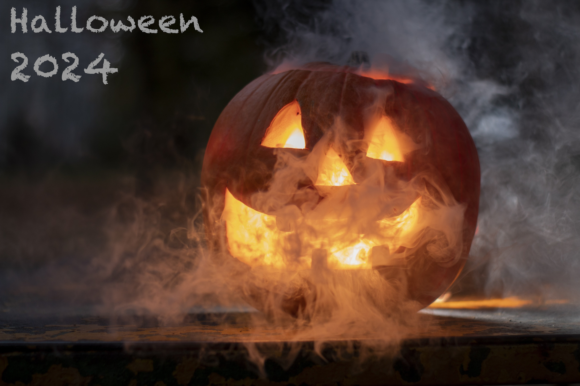 Carved pumpkin with a glowing face surrounded by smoke and "Halloween 2024" text.