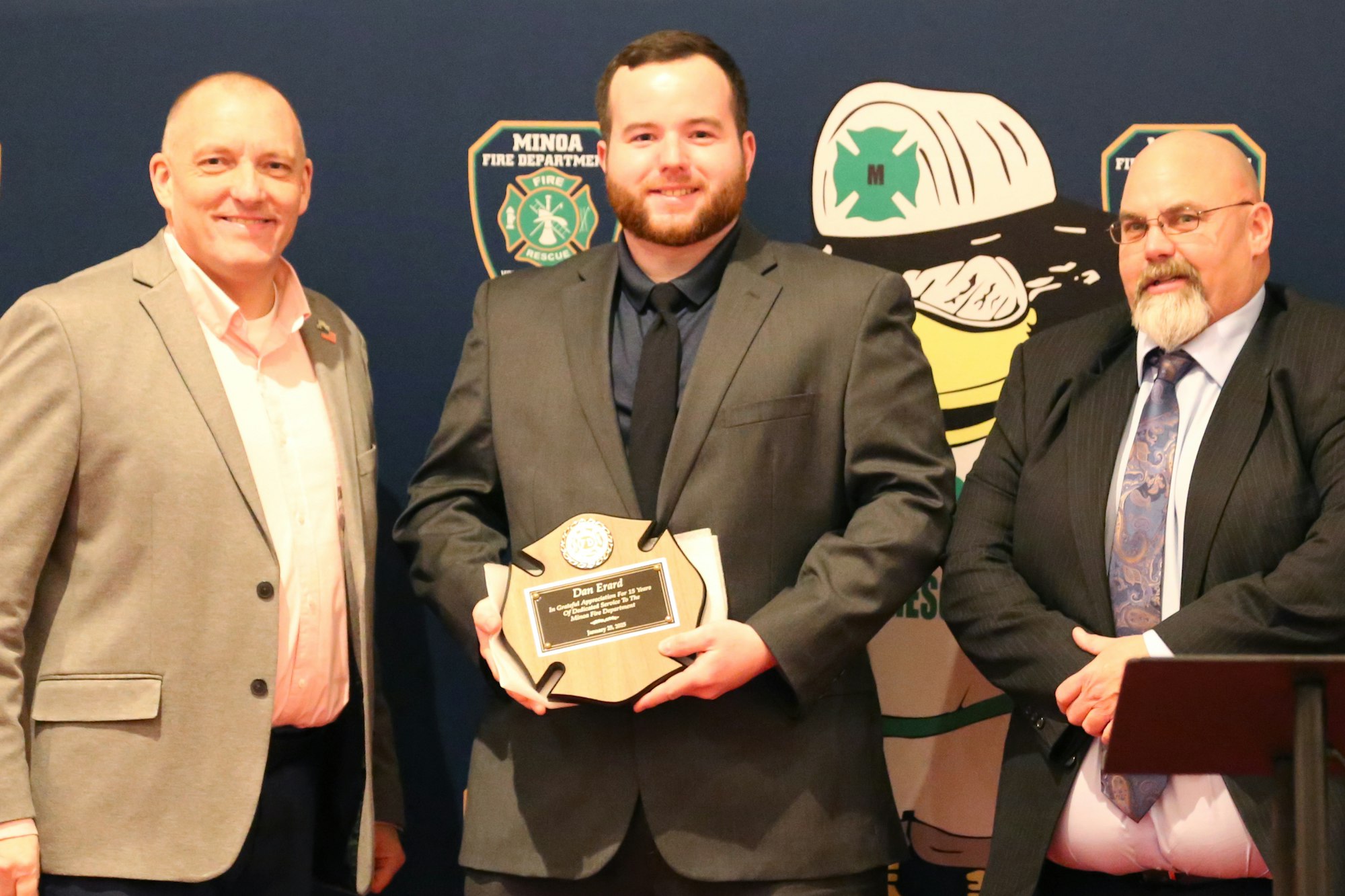 Chief Grevelding, Don Erard (holding his award), and President Tim Decker - Minoa Fire Department logos are in the background.