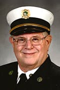 John, wearing a formal uniform with a white hat featuring a badge.
