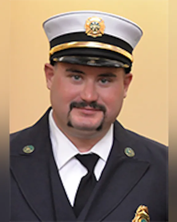 Deputy Chief Trevor VanAuken in his firefighter's dress uniform with a cap and badge.