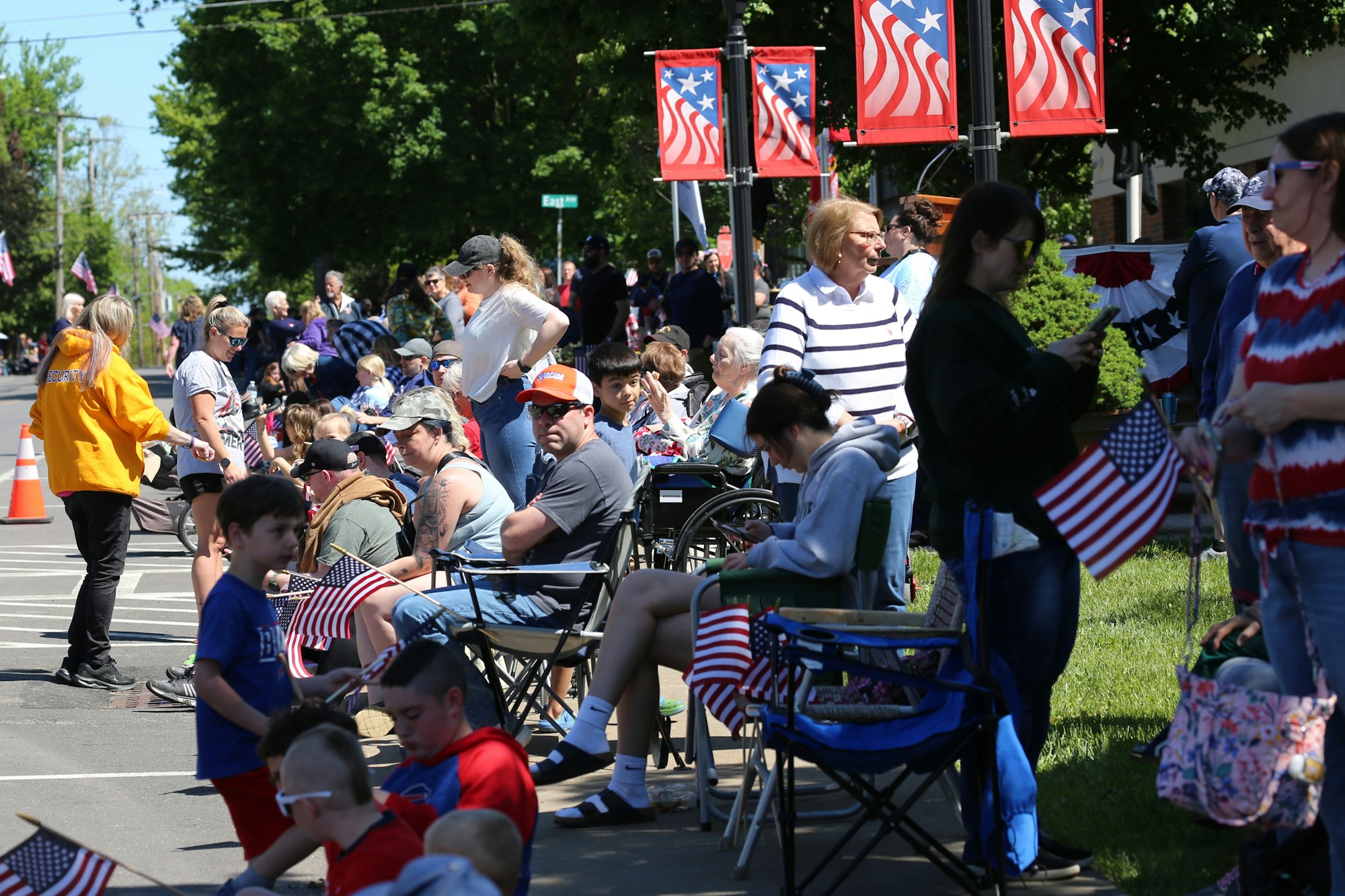 A crowd gathered on a street, holding American flags, with patriotic banners overhead.
