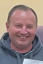 Erich Schepp smiling, wearing a hoodie, holding a piece of paper.
