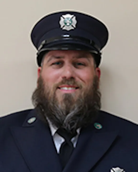 Kraig Marquart in a uniform with a cap with a badge, sporting a beard and smiling.